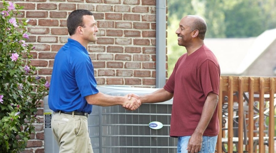 two men shake hands in front of an AC unit